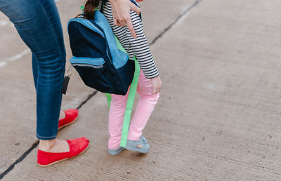 Low section of mother standing with schoolgirl on footpath