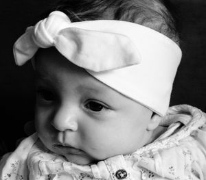 Close-up of baby wearing headband with bow against black background