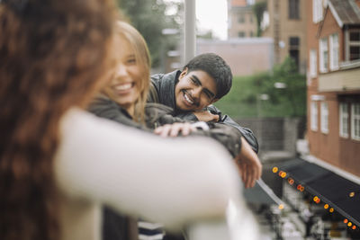 Smiling boy leaning on railing while watching female friends