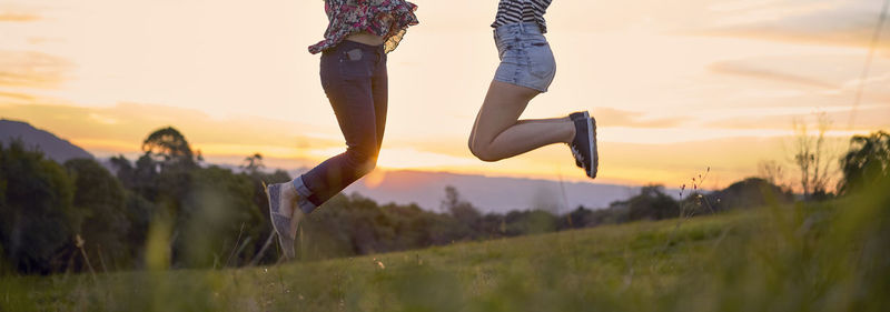 Low section of friends jumping over field against sky