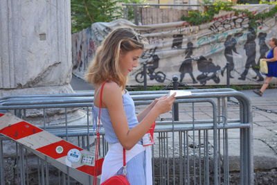 Side view of young woman standing against railing