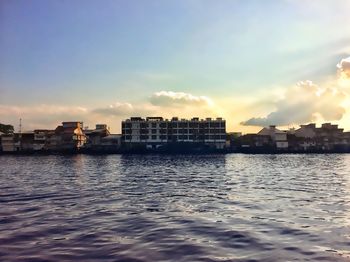 Buildings by sea against sky during sunset