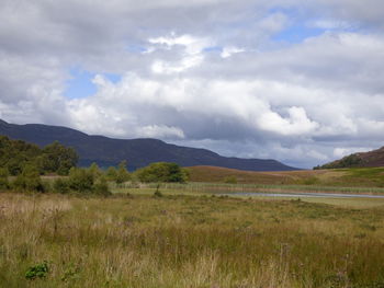 Scenic view of grassy field and mountains against cloudy sky