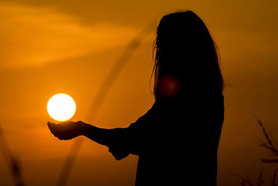 Silhouette of woman holding sun at sunset