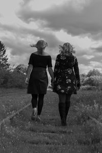 Rear view of friends walking on land against cloudy sky