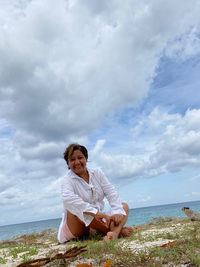 Woman sitting by sea against sky