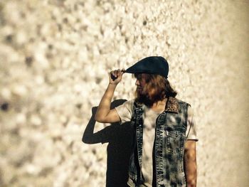 Man wearing flat cap while standing by concrete wall during sunny day