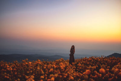 Woman standing on rock against sky during sunset