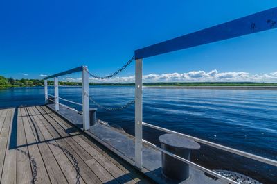 Railing on pier by sea against blue sky
