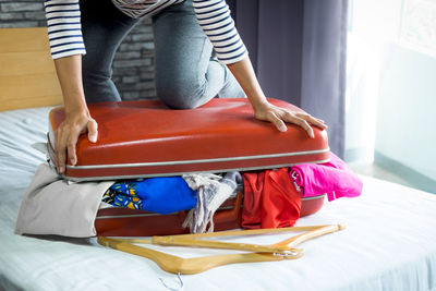 Low section of woman over luggage over bed at home