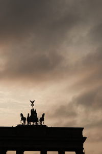 Low angle view of silhouette brandenburg gate against cloudy sky during sunset