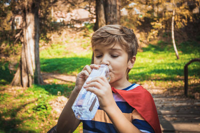 Boy drinking water from bottle in forest