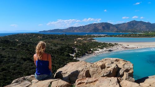 Woman sitting on rocks against mountain and blue sky