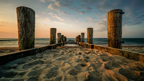 Wooden posts on beach against sky during sunset