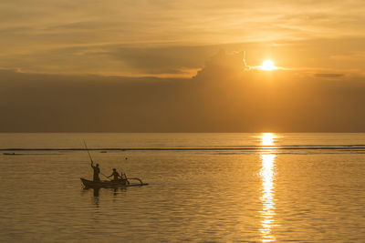 Silhouette men on boat in sea against sky during sunset