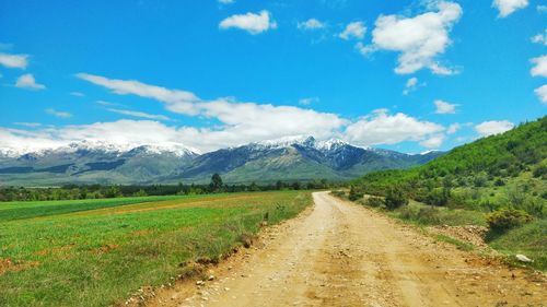 Dirt road along landscape and mountains against sky