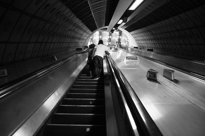 Rear view of people walking on escalator at subway station