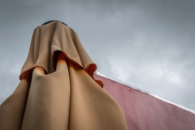 High section of folded parasol against cloudy sky