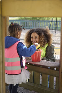 Smiling female teacher playing with girl in playhouse