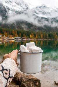 Picnic in bavarian mountains, germany. hand with mug of cacao and marshmallow on the lake background