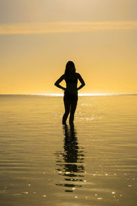 Silhouette woman standing on beach against sky during sunset