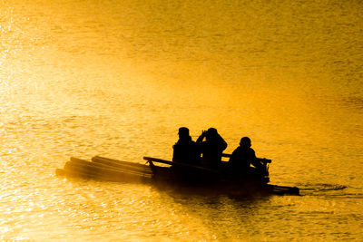 Silhouette people sitting on sea against orange sky