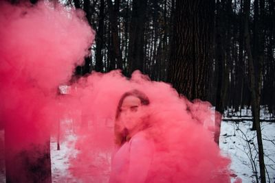 Young woman with smoke bomb standing in forest during winter