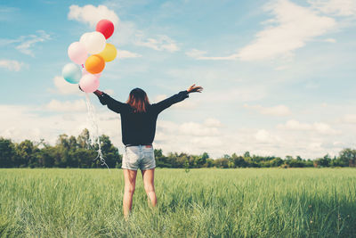 Rear view of woman with balloons standing on field against sky