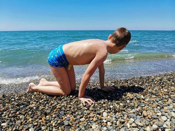 A boy in swimming trunks sits on the shore of the black sea after swimming