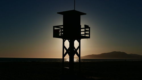 Silhouette cross on beach against sky during sunset