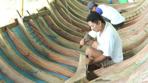 Side view of male workers making wooden boat