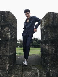 Portrait of young man standing on rock against sky