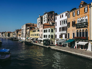 Buildings by canal against clear blue sky in city