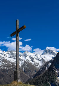 Low angle view of cross on snowcapped mountains against blue sky