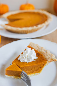 Traditional autumn pumpkin pie with the whipped cream on the plate close-up. thanksgiving dessert.