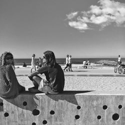 People relaxing at sea shore against sky