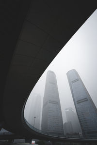 Low angle view of modern buildings against sky during foggy weather