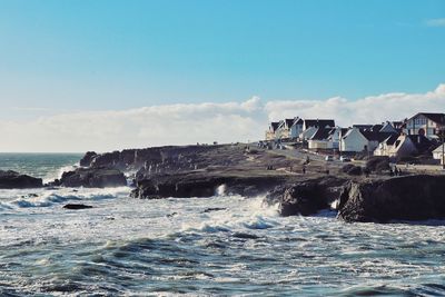 Scenic view of by sea splashing on rocks against sky