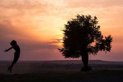 Silhouette man standing by tree against sky during sunset