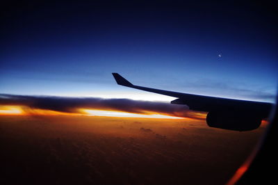 Airplane wing against clear sky during sunset
