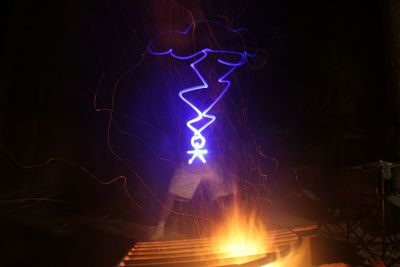 Person with light painting standing by campfire at night