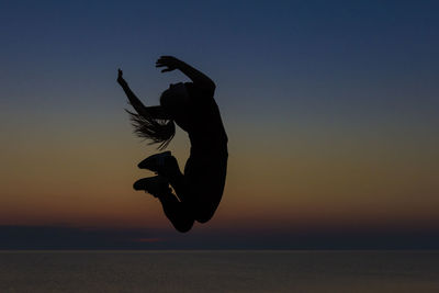 Silhouette man jumping in sea against sky during sunset