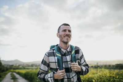 Smiling mature man with backpack hiking under sky