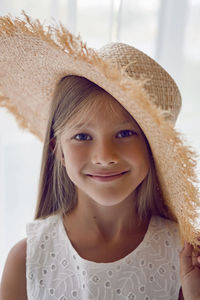 Girl in the straw hat stands at the window in the white room