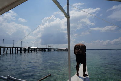 Rear view of woman standing by sea against sky