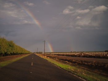 Road passing through field against cloudy sky