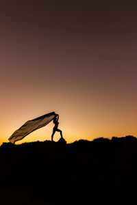 Silhouette woman with scarf standing on land during sunset