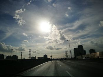 Road by city against cloudy sky on sunny day