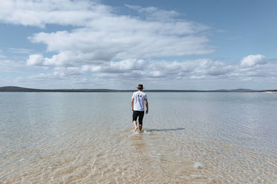 Rear view of man standing on beach against sky