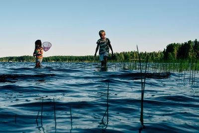 Boys standing on lake against clear sky